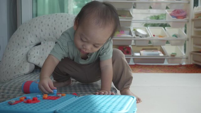 A toddler bends down to play with colorful building blocks, showcasing their curiosity and creativity. The bright setting suggests a playful environment, highlighting early childhood exploration.
