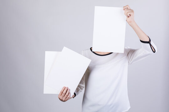 Woman holding blank white paper sheets with face covered in studio