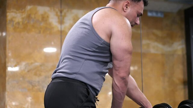 Side view of a strong muscular man performing bent over dumbbell rows for back muscle development in a modern fitness gym