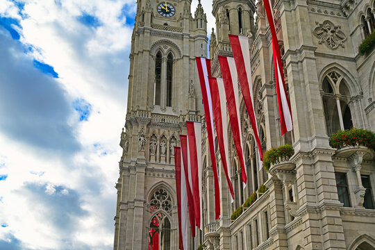 Low-angle view of the clock tower of Vienna City Hall with Austrian flags under a dramatic sky, Vienna
