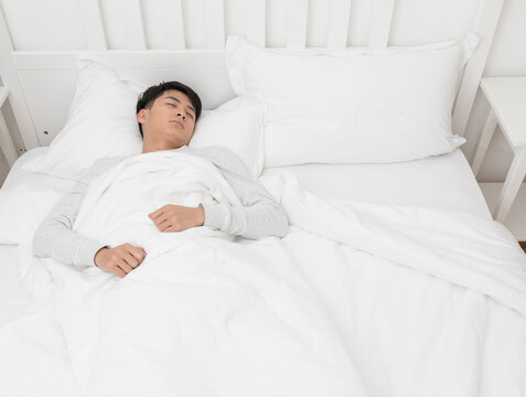 Young man sleeping peacefully in white bed at home