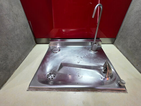 Stainless steel drinking fountain and water bottle refill station in a public building. Modern recessed design features a tall faucet and metallic bubbler against a vibrant red wall panel.