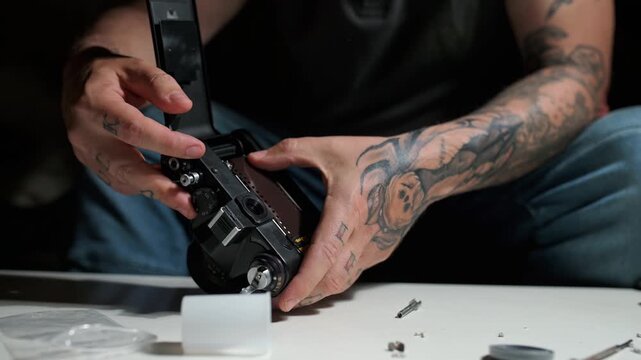 Close up of a tattooed man's hands carefully loading a 35mm film roll into a classic analog camera after completing a repair