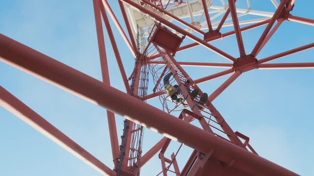 Workers are seen climbing a tall communication tower against a bright blue sky. The scene conveys a sense of industry and teamwork.