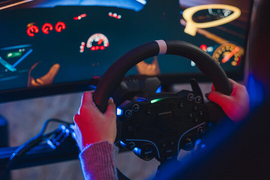 Woman playing game while driving car in virtual simulator with steering wheel and display screen indoors during entertainment activity
