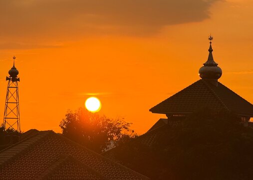 Beautiful sunset over mosque dome and minaret with orange sky and sun, silhouette of Islamic architecture at dusk.
