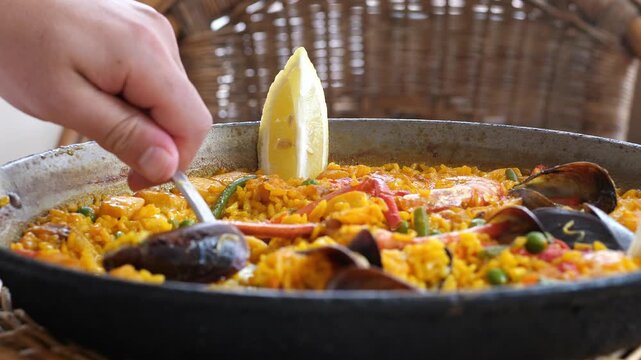 Close-up of a person eating traditional Spanish seafood paella with yellow rice, mussels, and prawns served fresh in a pan with lemon