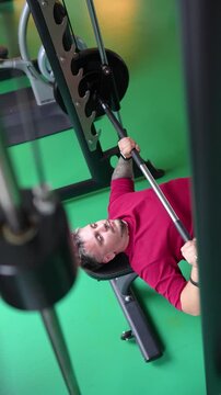 Confident sportsman doing bench press exercise with heavy barbell in smith fitness machine at gym, motivated male athlete in sports hall on bench making chest press weight lifting for muscle strength.