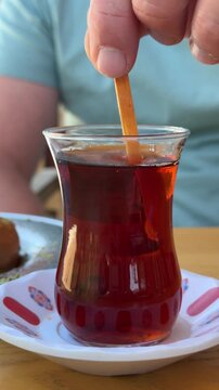 Man stirring Turkish black tea in a traditional tulip-shaped glass. Turkish culture, hospitality, authentic beverage, local traditions and travel experience concept.High quality 4k footage