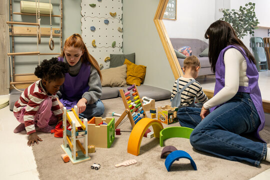 Educators are helping children play with educational wooden toys on a rug in a kindergarten