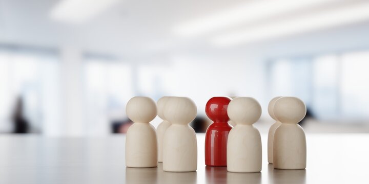 Wooden figures standing in circle around red figure on table in front of bright office background, team, leadership or manager business concept, selective focus