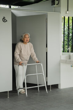 Shower safety solutions elderly concept. Elderly person adjusting a white shower chair in a bright, accessible bathroom with tiled walls.