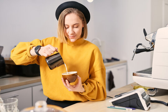 Barista pouring milk, making latte art, working at coffee shop