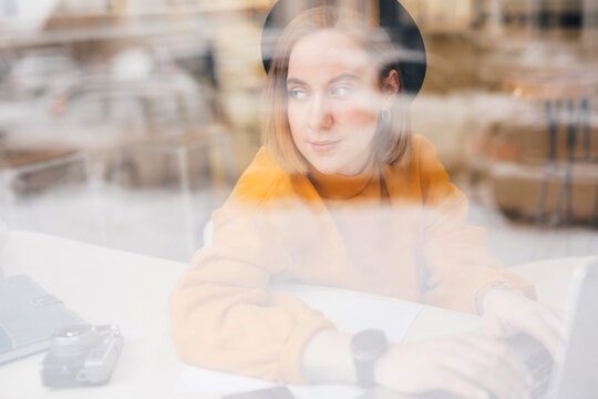 Woman using laptop, working in cafe, see through the window