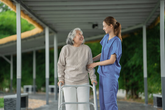 Young asian female caregiver helping happy elderly senior woman walk with walker outdoors in suburban neighborhood during autumn, support assistance and compassionate nursing for old age