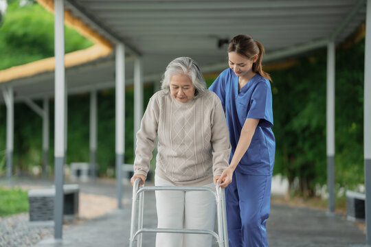 Young asian female caregiver helping happy elderly senior woman walk with walker outdoors in suburban neighborhood during autumn, support assistance and compassionate nursing for old age