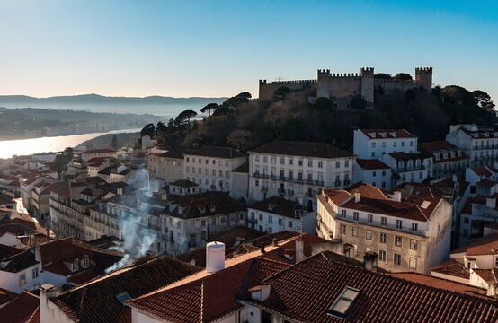 Historic sao jorge hilltop fortress overlooking red tiled rooftops, white facades, river reflections and rolling hills in picturesque European cityscape scenery generate ai