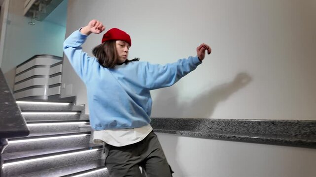 Young Woman in Red Beanie Freestyle Dancing Hip Hop on a Staircase in a Modern Building Lobby