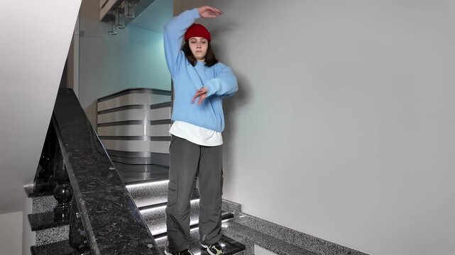 Young Woman in Red Beanie Freestyle Dancing Hip Hop on a Staircase in a Modern Building Lobby