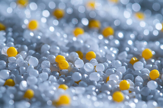 Macro shot of small translucent and yellow plastic polymer granules used in industrial manufacturing, showcasing the texture and reflective surface. Abstract background of polypropylene and