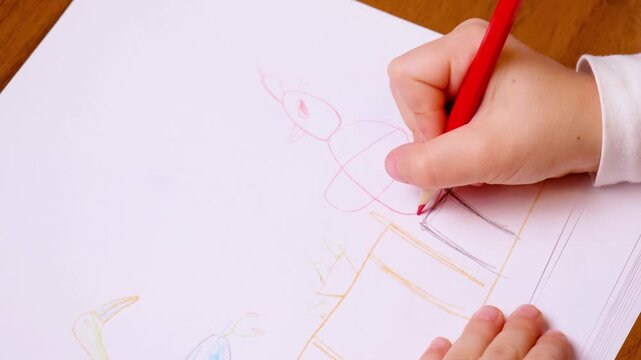 Child hand draws with red pencil on school paper. Small fingers grip tightly while tracing colorful shapes, showing fine motor practice, creativity, and back to school learning with pencil control