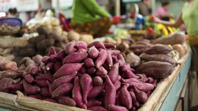 Close-up of fresh raw sweet potatoes and root vegetables displayed on a market stall at Xom Moi Market in Nha Trang, Vietnam. Commercial food supply and retail trade concept.