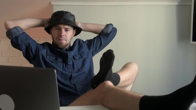 Young man shifts from relaxed pose to brief rest while working at laptop in modern home interior, with man, male, young, adult detail, showing relaxed, resting, focused, contemplative context
