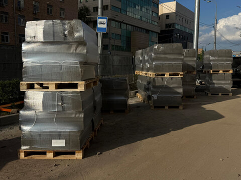 Plastic wrapped stacks of curb stones on a street. Urban roadworks concept. Handheld smartphone photo, selective focus, harsh sunlight, not AI
