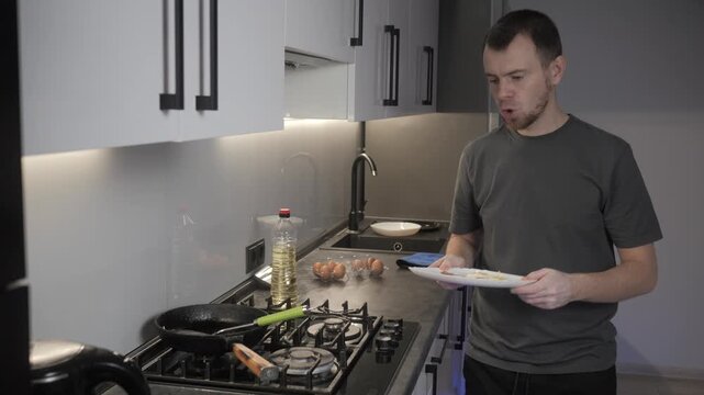 Man handling eggs beside gas cooktop in modern kitchen with cast iron skillet, open carton, oil bottle, white bowl, reflective backsplash, and focused preparation for cooking