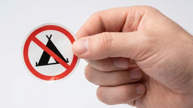 Hand holding a circular no camping prohibition sticker isolated on white