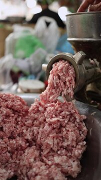 Close-up of a commercial meat grinder processing raw minced pork falling into a steel bowl at Xom Moi Market in Nha Trang, Vietnam. Food supply, butchery processing and retail market trade.