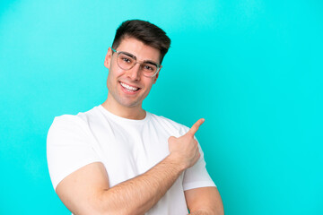 Fototapeta premium Young caucasian man isolated on blue background With glasses and pointing side