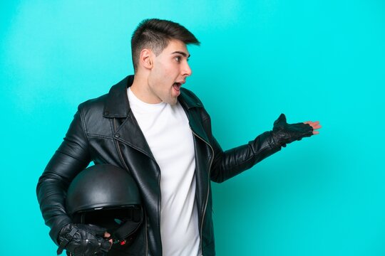 Young caucasian man with a motorcycle helmet isolated on blue background with surprise expression while looking side