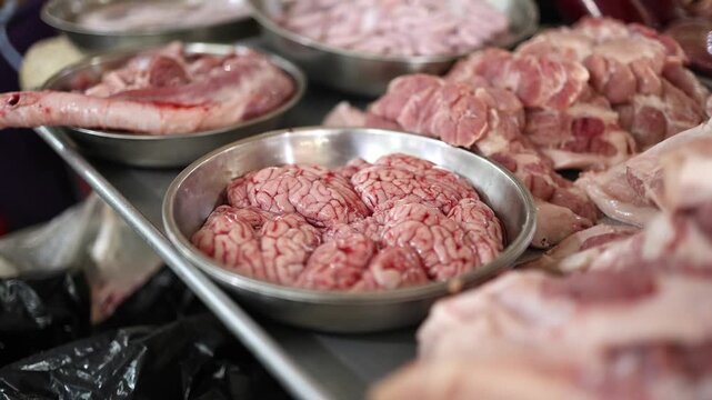 Close-up of fresh raw pork brains and offal displayed in steel bowls for sale on a meat stall at Xom Moi Market in Nha Trang, Vietnam. Commercial food supply and local retail trade concept.
