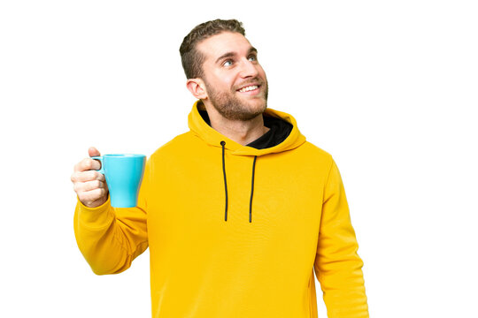 Young handsome blonde man holding cup of coffee over isolated background looking up while smiling