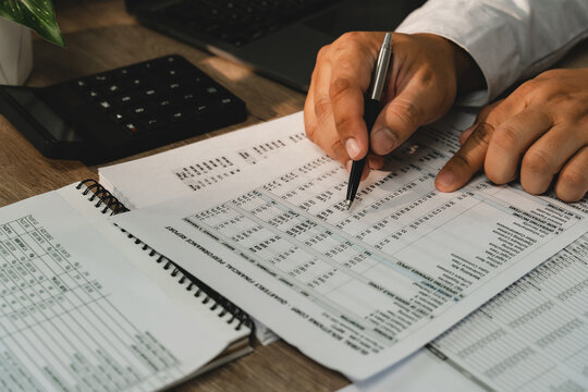 Accountant reviewing financial report with pen beside calculator and laptop for accounting, audit, tax preparation, bookkeeping, financial planning.