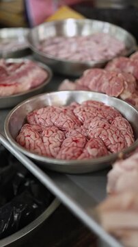 Close-up of fresh raw pork brains and offal displayed in steel bowls for sale on a meat stall at Xom Moi Market in Nha Trang, Vietnam. Commercial food supply and local retail trade concept.