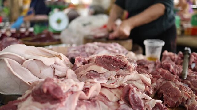 Close-up of fresh raw pork meat, cuts and offal displayed on a stall at Xom Moi Market in Nha Trang, Vietnam, with a vendor butchering in the background. Commercial food supply and retail trade.
