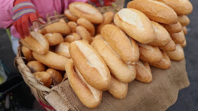 Close-up of fresh crispy Vietnamese baguettes or banh mi stacked in wicker baskets for sale at Xom Moi Market in Nha Trang, Vietnam. Local bakery, street food supply and retail trade concept.