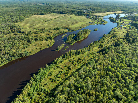 Aerial view of a winding river meandering through green taiga forest and fields near Kindasovo village in Karelia, Russia