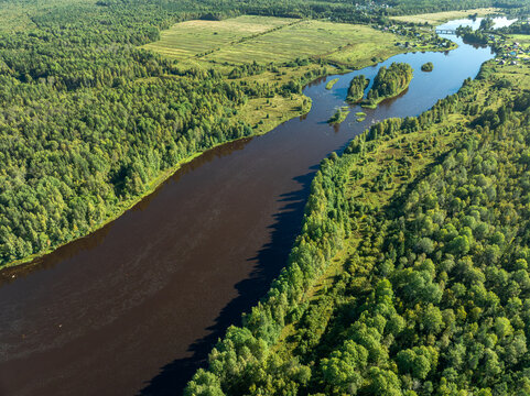 Aerial view of a winding river meandering through green taiga forest and fields near Kindasovo village in Karelia, Russi