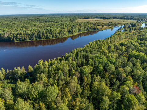 Aerial view of a winding river meandering through green taiga forest and fields near Kindasovo village in Karelia, Russi