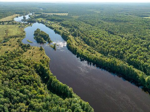 Aerial view of a winding river meandering through green taiga forest and fields near Kindasovo village in Karelia, Russi