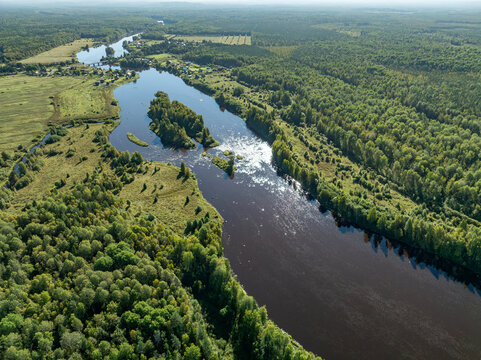 Aerial view of a winding river meandering through green taiga forest and fields near Kindasovo village in Karelia, Russia