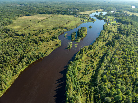 Aerial view of a winding river meandering through green taiga forest and fields near Kindasovo village in Karelia, Russia