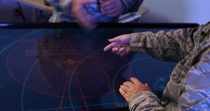 Military personnel use a touchscreen command table with a radar-style map, planning operations in a dark control room.