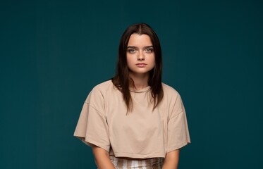 Naklejka premium Young woman with neutral expression posing, wearing casual crop top against a teal background