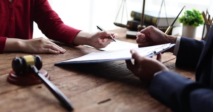 Lawyer and client discussing a contract agreement, financial paperwork, or legal document with a gavel and pen on a rustic wooden desk, offering legal advice