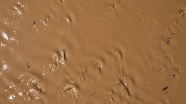 Wet brown mud texture background. Top down view of liquid soil surface after heavy rain.