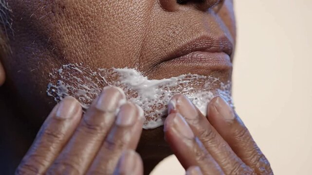 Middle aged woman with deep complexion applying white facial cream on chin area for morning skincare routine, focus on skin texture and hydration product application steps